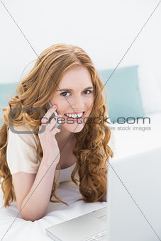 Casual woman using laptop and cellphone in bed