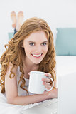 Smiling blond with coffee cup using laptop in bed