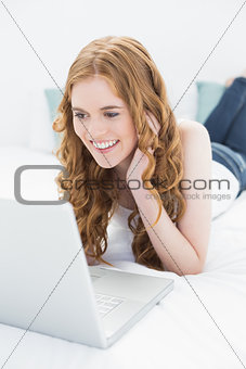 Smiling casual blond using laptop in bed