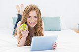 Casual blond using tablet PC while holding an apple in bed