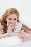 Worried woman looking at pills in bed