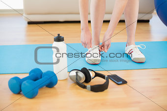 Female tying shoes with sporty equipment in fitness center