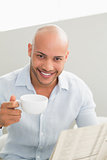 Smiling man having coffee while reading newspaper