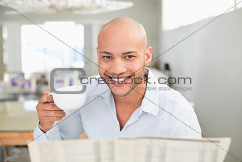 Smiling man with coffee cup reading newspaper at home