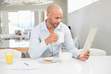 Man drinking coffee while reading newspaper at home