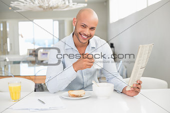Smiling man drinking coffee while reading newspaper at home