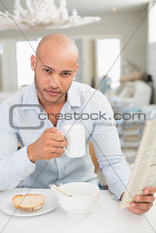 Man drinking coffee while reading newspaper at home
