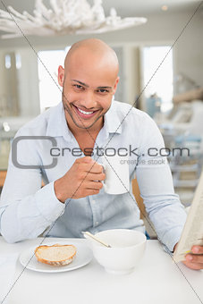 Smiling man drinking coffee while reading newspaper at home
