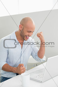 Smiling casual young man using laptop at home