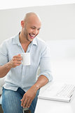 Cheerful man with laptop drinking coffee at home