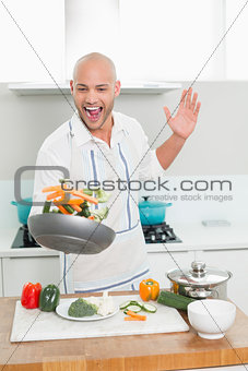Cheerful man tossing vegetables in the kitchen