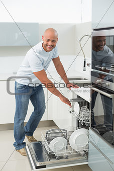 Smiling young man using dish washer in kitchen