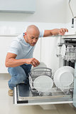 Serious man using dish washer in kitchen
