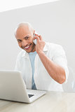 Casual smiling man using cellphone and laptop at desk