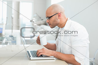 Concentrated casual man with coffee cup using laptop at home