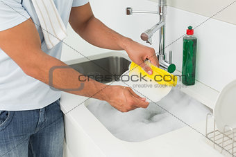 Mid section of a man doing the dishes at kitchen sink
