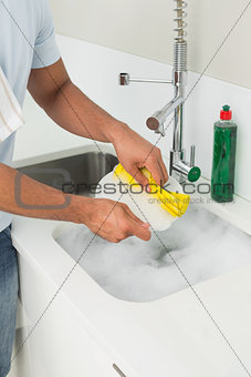 Mid section of man doing the dishes at kitchen sink