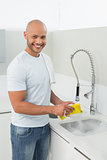 Smiling young man doing the dishes at kitchen sink