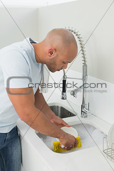 Young man doing the dishes at kitchen sink