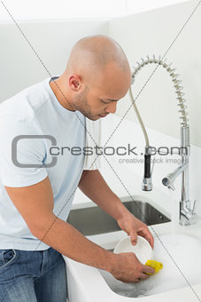Young man doing the dishes at kitchen sink