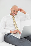 Smiling businessman using laptop on sofa at home