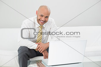 Smiling businessman using laptop on sofa at home