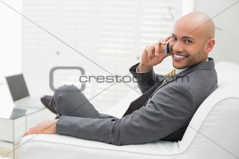 Smiling elegant businessman using cellphone on sofa at home