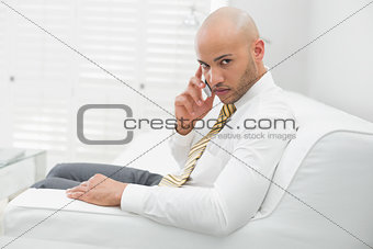 Serious businessman using cellphone on sofa at home