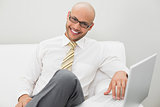 Smiling elegant businessman using laptop on sofa at home