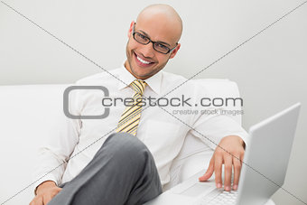 Smiling elegant businessman using laptop on sofa at home