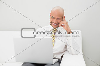 Elegant businessman with laptop sitting on sofa at home