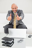 Elegant businessman gesturing thumbs up with laptop at home