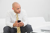 Thoughtful businessman with mobile phone on sofa at home