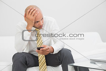 Thoughtful businessman with mobile phone sitting on sofa