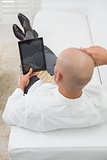 Bald businessman using digital tablet on sofa at home