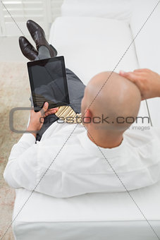 Bald businessman using digital tablet on sofa at home