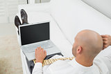 Bald businessman using laptop on sofa at home