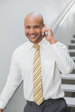 Smiling businessman using cellphone against staircase
