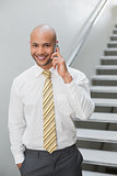 Smiling businessman using cellphone against staircase