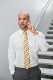 Serious businessman using cellphone against staircase