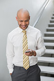 Smiling businessman text messaging against staircase