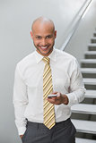 Smiling businessman text messaging against staircase