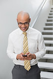 Smiling businessman text messaging against staircase in office