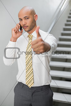 Businessman using cellphone and gesturing thumbs up