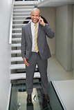Elegant businessman using cellphone against staircase in office