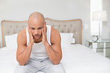 Thoughtful bald man sitting on bed