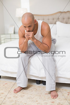 Thoughtful young bald man sitting on bed