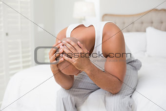 Thoughtful bald man with head in hands on bed