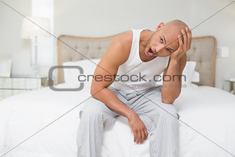 Bald man sitting and yawning in bed