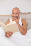 Smiling relaxed bald man reading book in bed